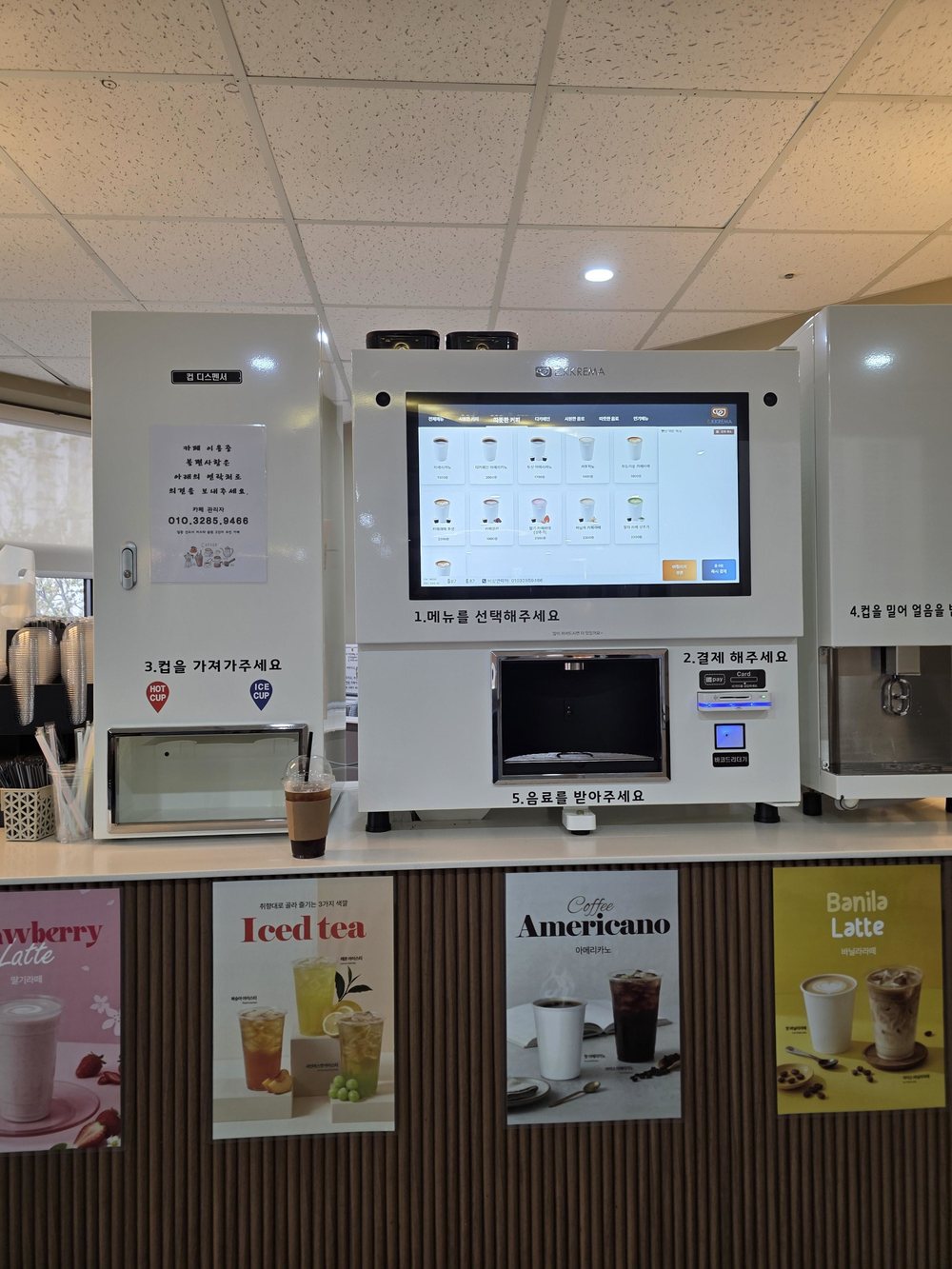 메뉴 포스터를 붙인 카운터 위의 유로 무인카페머신과 제빙기, 컵 디스펜서